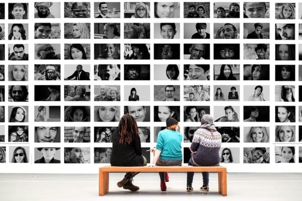 3-people-sitting-in-front-of-a-wall-of-pictures-of-people
